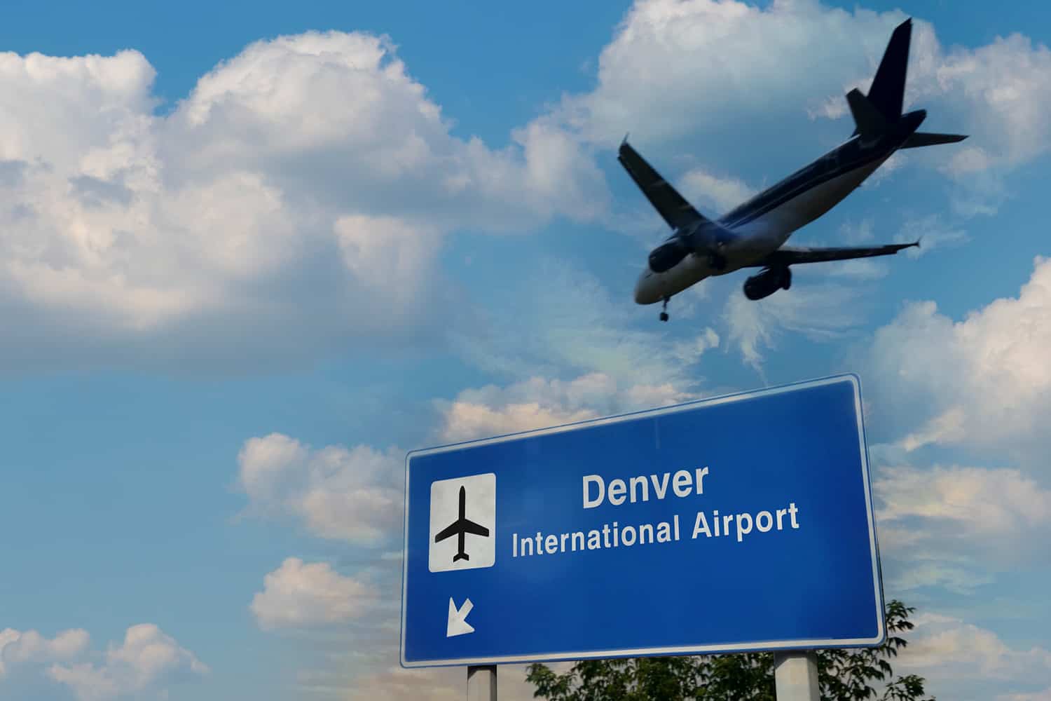 road sign that says Denver International Airport with plane flying overhead
