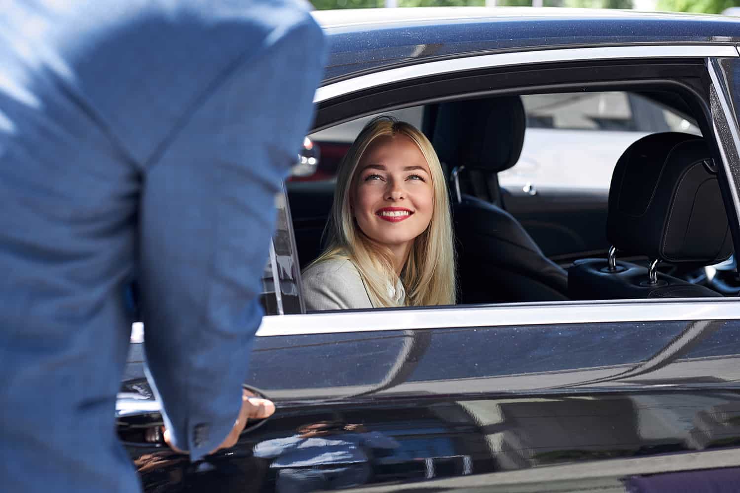 smiling passenger in car as chauffeur opens the door